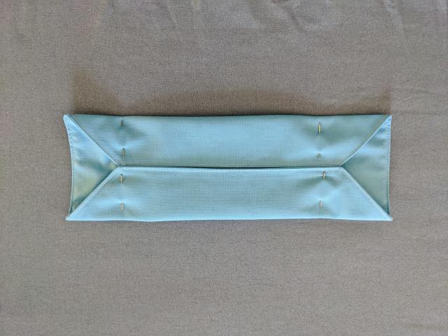 blue fabric mask with long sides folded to meet in the center and secured by four pins