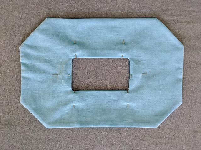 Blue fabric mask with inside square aligned and pinned with straight pins.