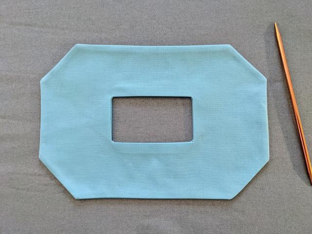 Blue mask turned right-side out with no visible seams and sharp lines. A copper double sided knitting needle is next to it.