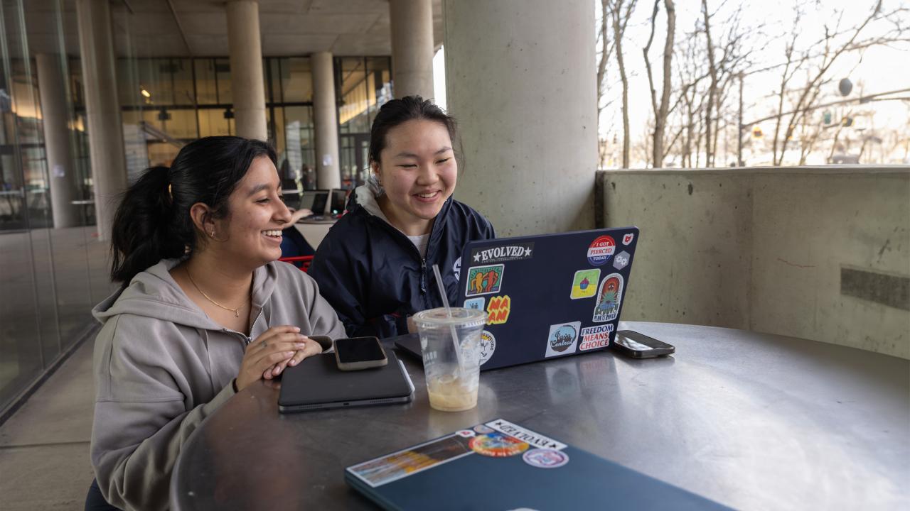 Two students discuss homework over a laptop at an outdoor cafe at the Knowlton School of Architecture